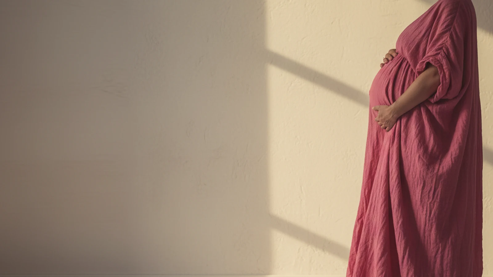 Schwangerer Bauch im Profil vor warmer weisser Wand, Golden Hour